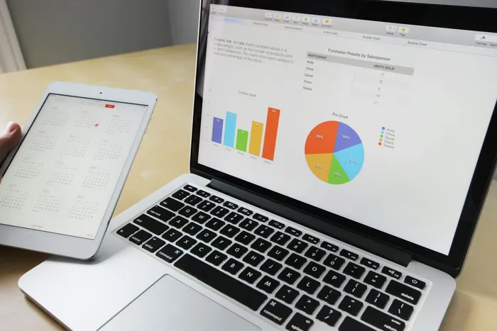 A laptop displaying various charts and graphs alongside an iPad showing a calendar, suggesting a focus on data analysis and organization.