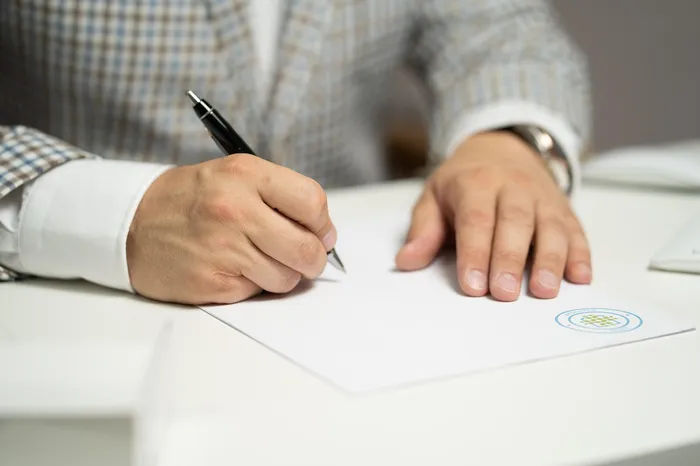 A person writing on a blank piece of paper with a pen, likely signing a document, demonstrating a professional setting.