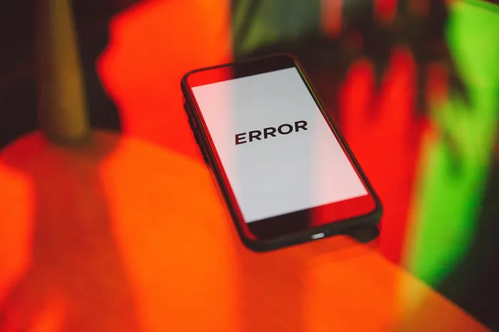 A smartphone displaying an 'ERROR' message on a white screen, laying on a reflective surface with colorful lighting.